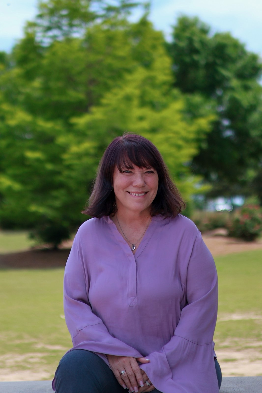 Beth Ali smiling outdoors in a lavender shirt